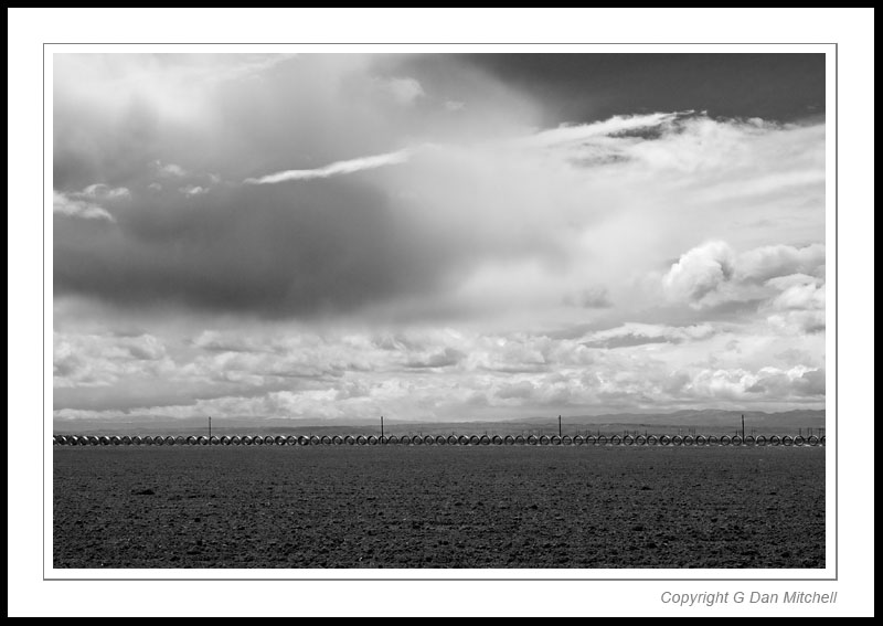 PipesWiresClouds2006|04|05: Pipes, Wires, Clouds. Near Wasco, Central Valley, California. April 5, 2006. &copy; Copyright G Dan Mitchell.