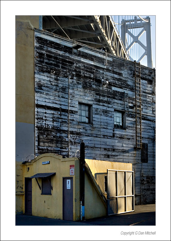 YellowWharfShack2006|07|20: Yellow Shack on the Embarcadero. San Francisco, California. July 20, 2006. &copy; Copyright G Dan Mitchell.    keywords: yellow shack building wall san francisco bay bridge color photograph embarcadero