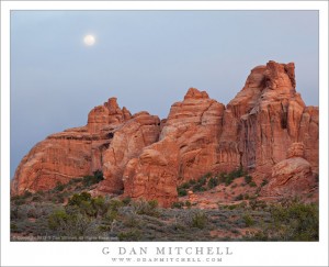 The full moon rises in a cloudy sky above sandstone towers, Arches National Park, Utah.